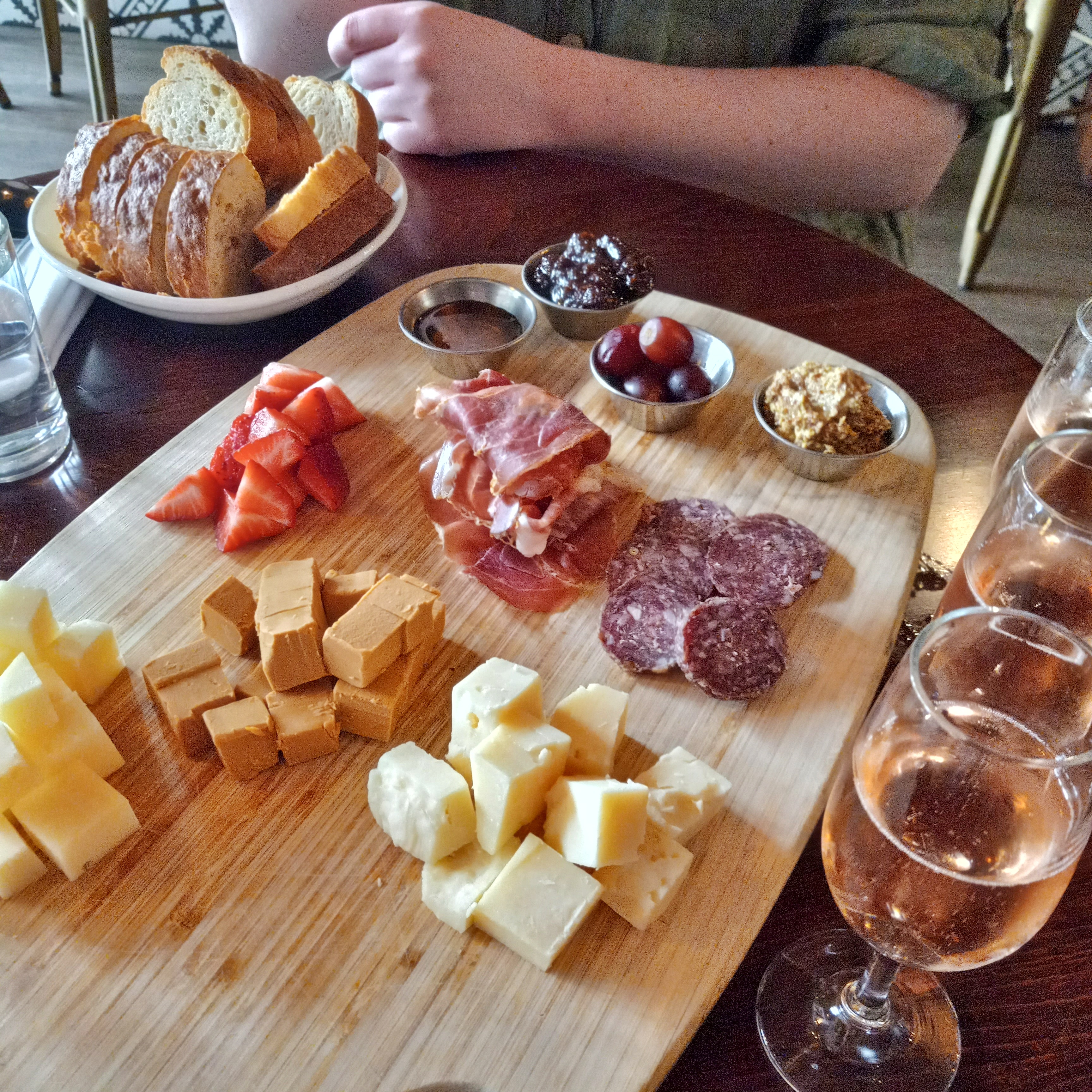 A board with assorted meats and cheeses next to a bowl of bread slices