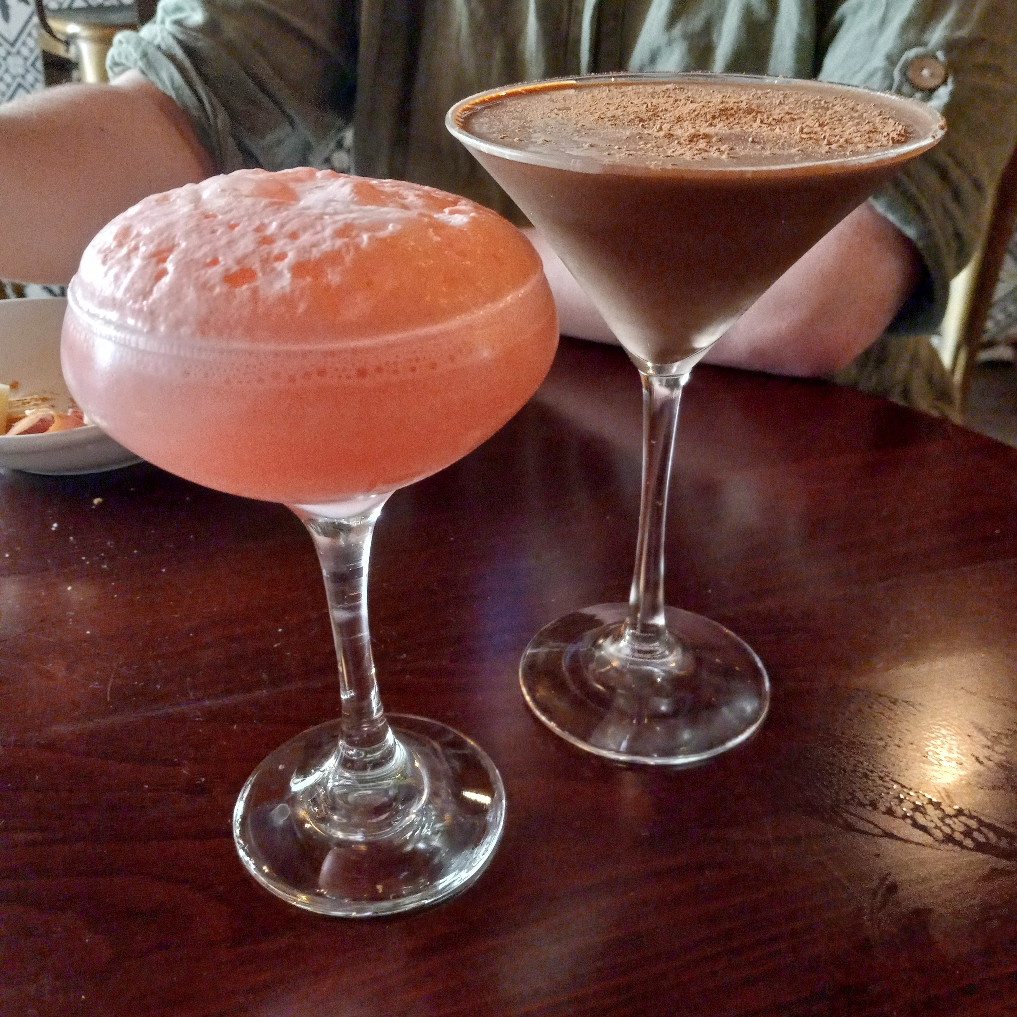 A pink cocktail with lots of foam on top and a brown coktail with chocolate dust on top